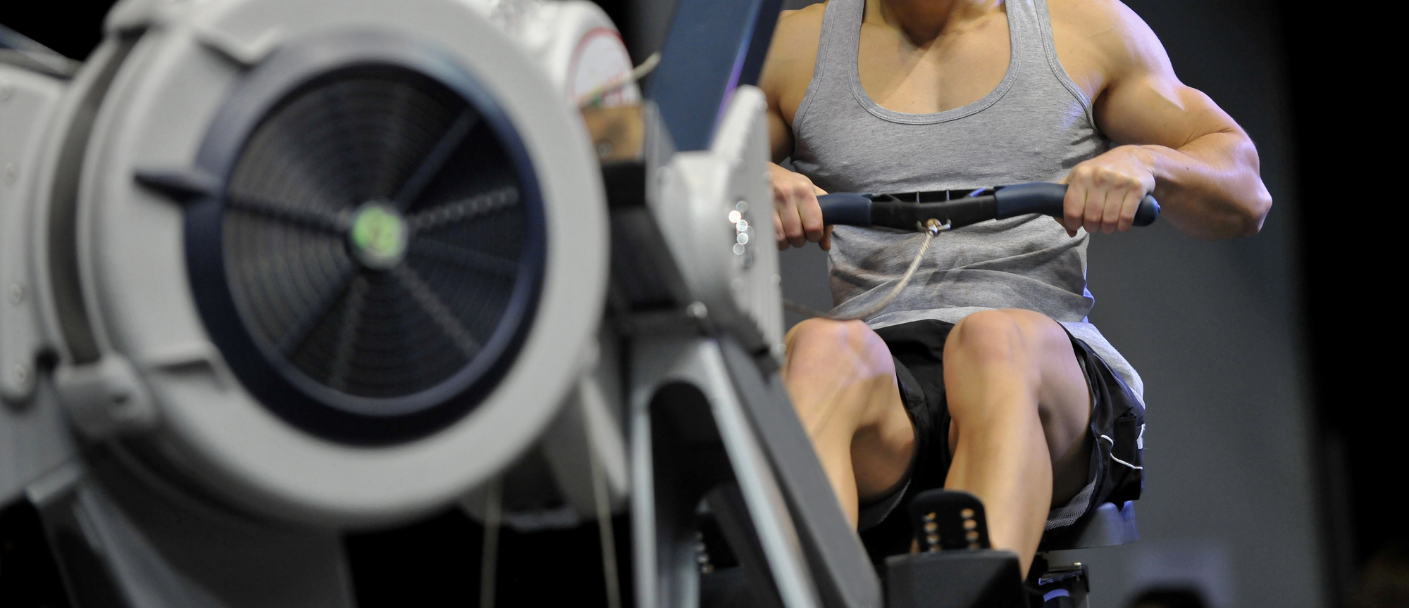 Powerful muscular man CrossFit trainer do workout on indoor rower at the gym